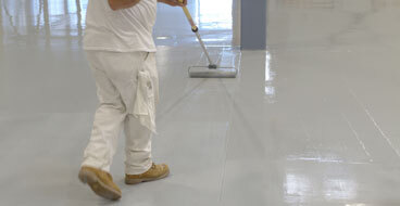 Fast Professional Installation This image shows a man painting an industrial floor using a paint roller.