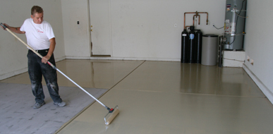 This image shows a man painting a floor with a roller brush.