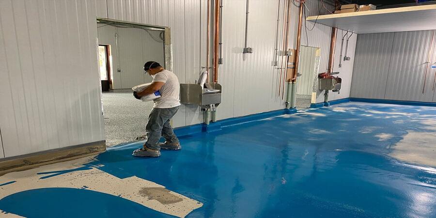 epoxy-concrete-floor-coating This image shows a man painting a floor.