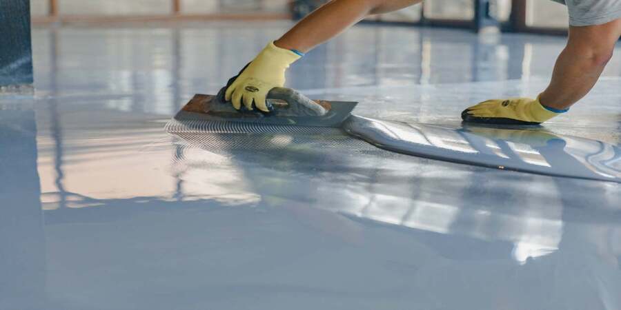 concrete-epoxy-coating This image shows a man applying epoxy on a floor.